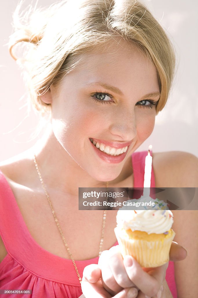 Young woman holding cupcake with burning candle, portrait, smiling