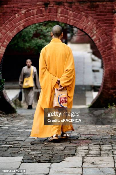 shaolin monk holding fast-food bag behind back, outside temple entrance - monks of shaolin temple stock pictures, royalty-free photos & images