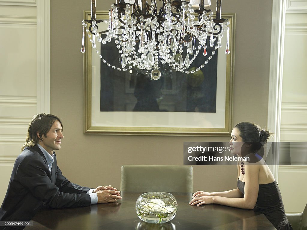 Couple sitting on opposite sides of table in luxurious room, side view