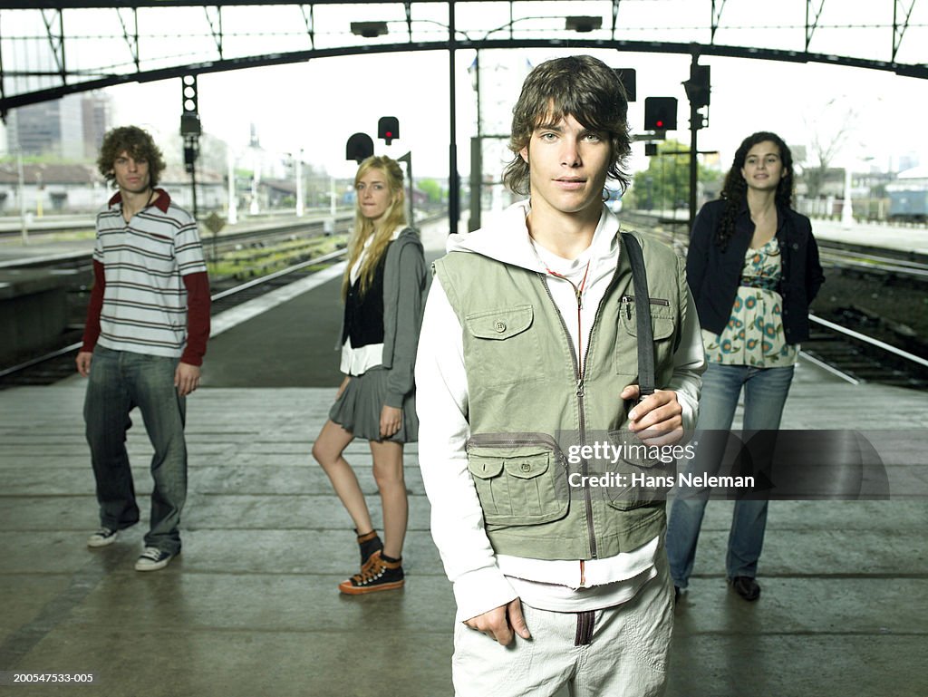 Young man with friends at railway station, posing, three quarter length