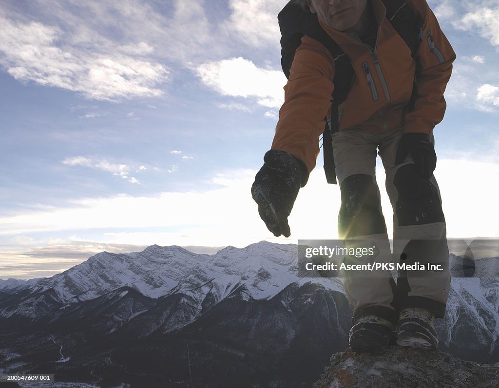 Mountaineer standing on mountain top, extending arm, low section