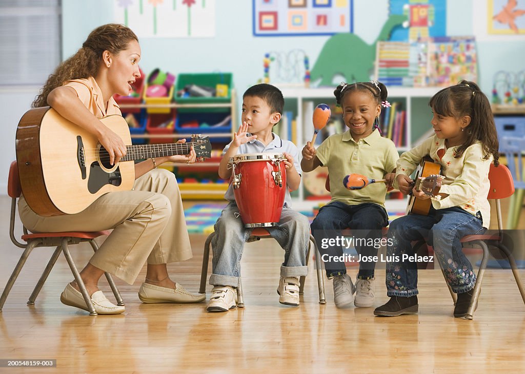 Schoolchildren (4-5) playing musical instruments with teacher in classroom