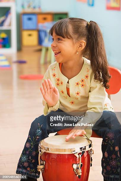 schoolgirl (4-5) playing conga in classroom, smiling - conga stock pictures, royalty-free photos & images