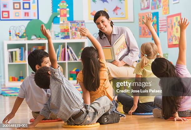 teacher reading book in classroom, children (2-7) raising hands - preschool age stock pictures, royalty-free photos & images