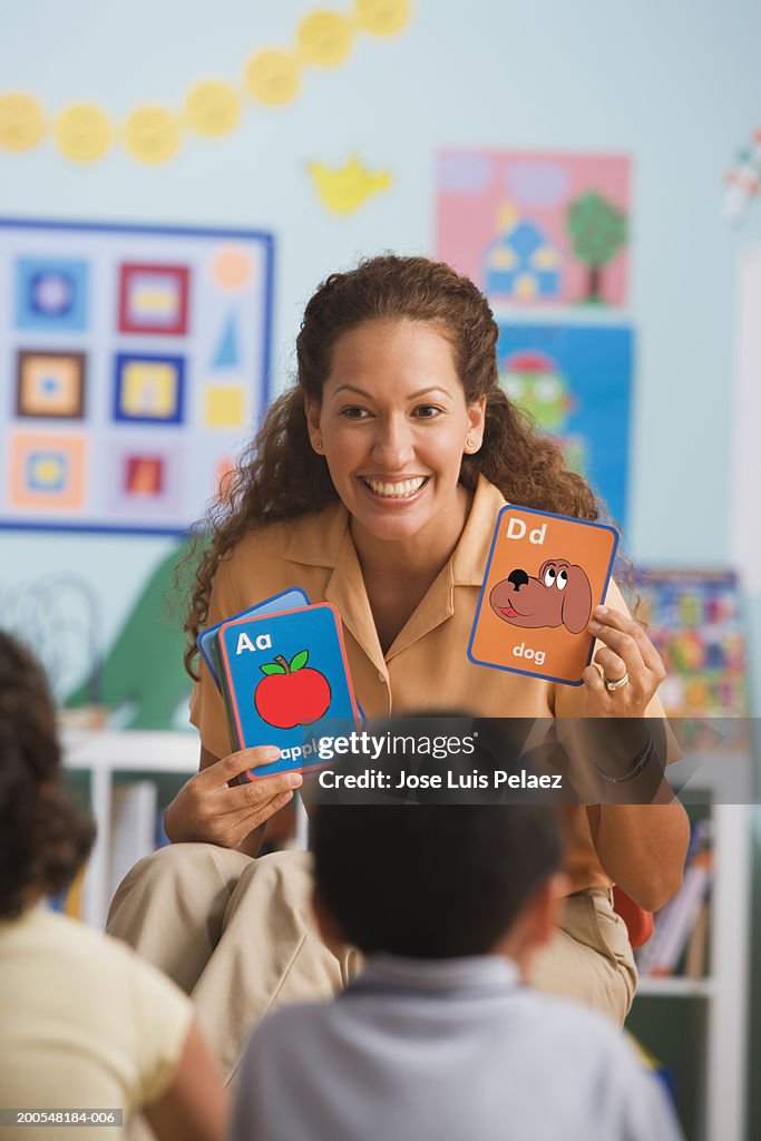 Teacher holding up flash card in classroom, smiling