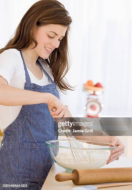 young woman stirring ingredients in mixing bowl, smiling, side view - whipping woman stock pictures, royalty-free photos & images