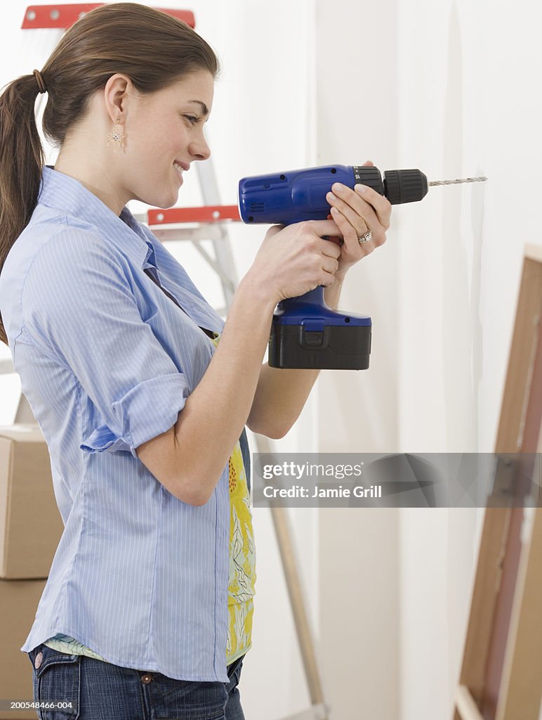 Young woman drilling wall, smiling, side view