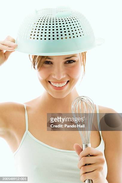 young woman with colander  on head, holding whisk, smiling, close-up - ballonklopper stockfoto's en -beelden