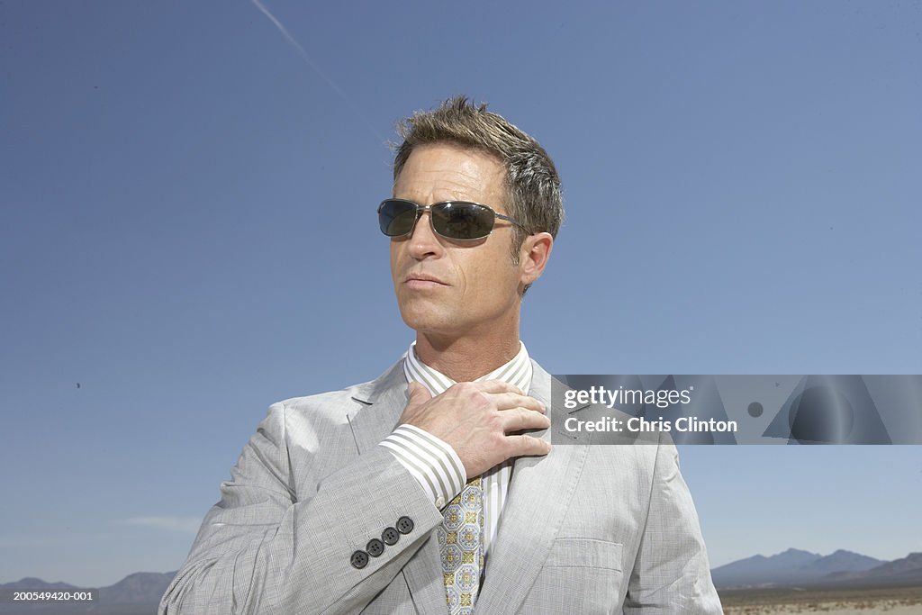 Businessman in dry lake bed holding hand to collar