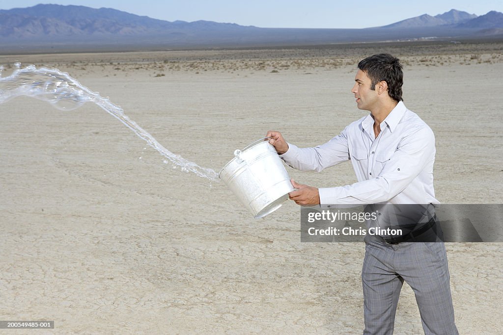 Businessman throwing bucket of water on dry lake bed