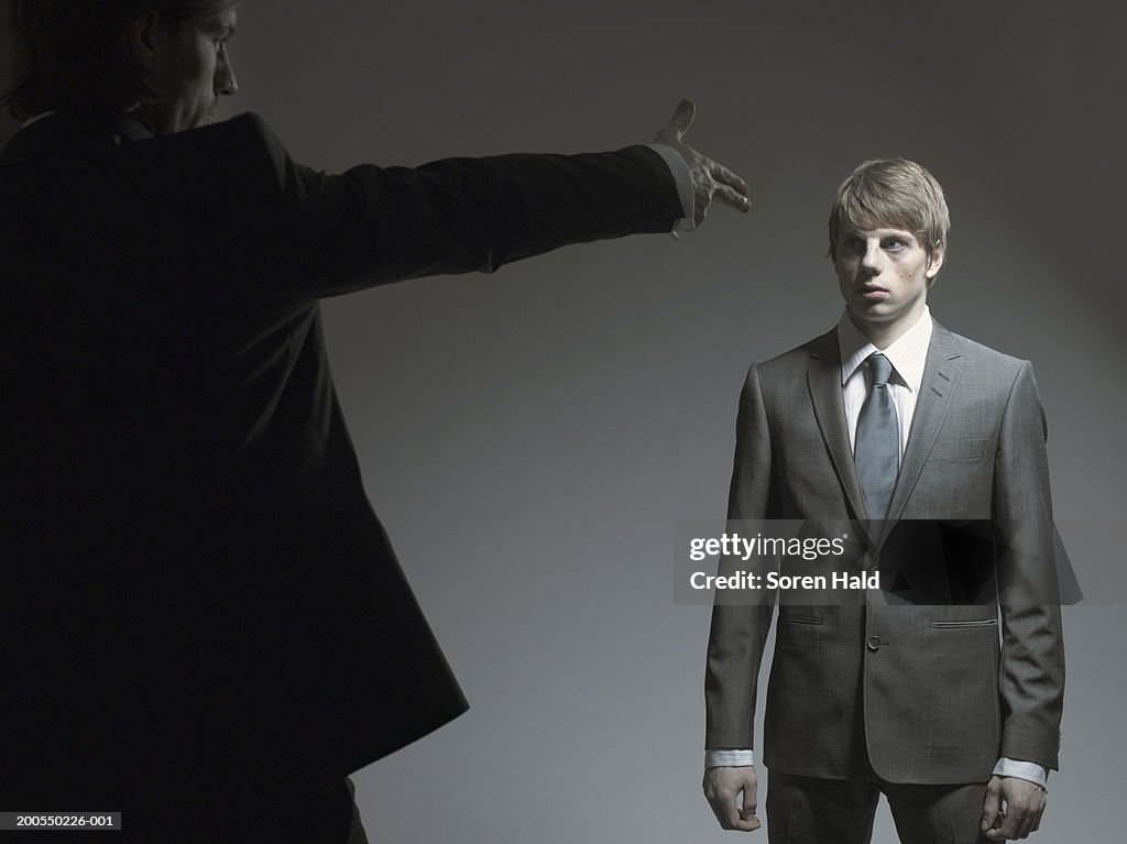 Businessman pointing finger gun at young man