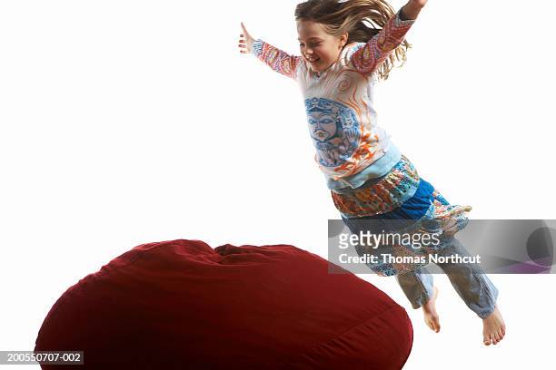 girl (7-9) jumping onto bean bag, arms outstretched - ビーズソファ ストックフォトと画像