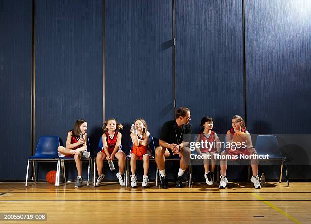 coach and girls (8-10) sitting on chairs beside basketball court - vereinscoaching stock-fotos und bilder