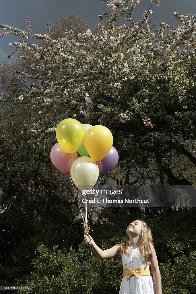 Girl (8-10) holding bunch of balloons outdoors, head back, smiling
