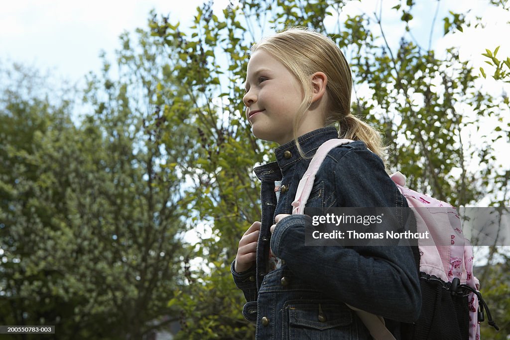 Girl (8-10) carrying backpack outdoors, smiling, side view