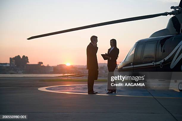 silhouette of businessman and woman standing by helicopter, side view - helipad stock pictures, royalty-free photos & images