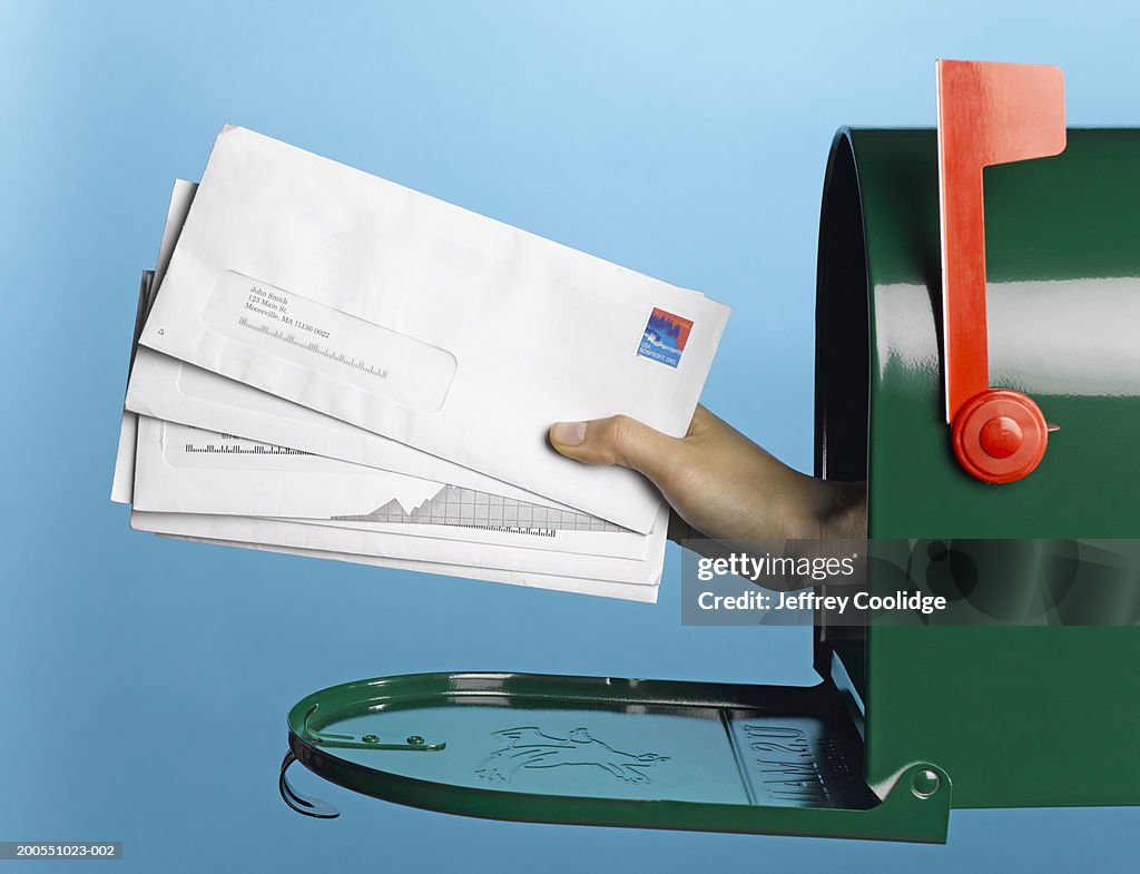 Young woman holding mail out of mailbox, side view