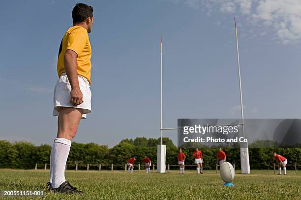 rugby player in field preparing to kick ball from tee, side view - rugby ball kick stock pictures, royalty-free photos & images
