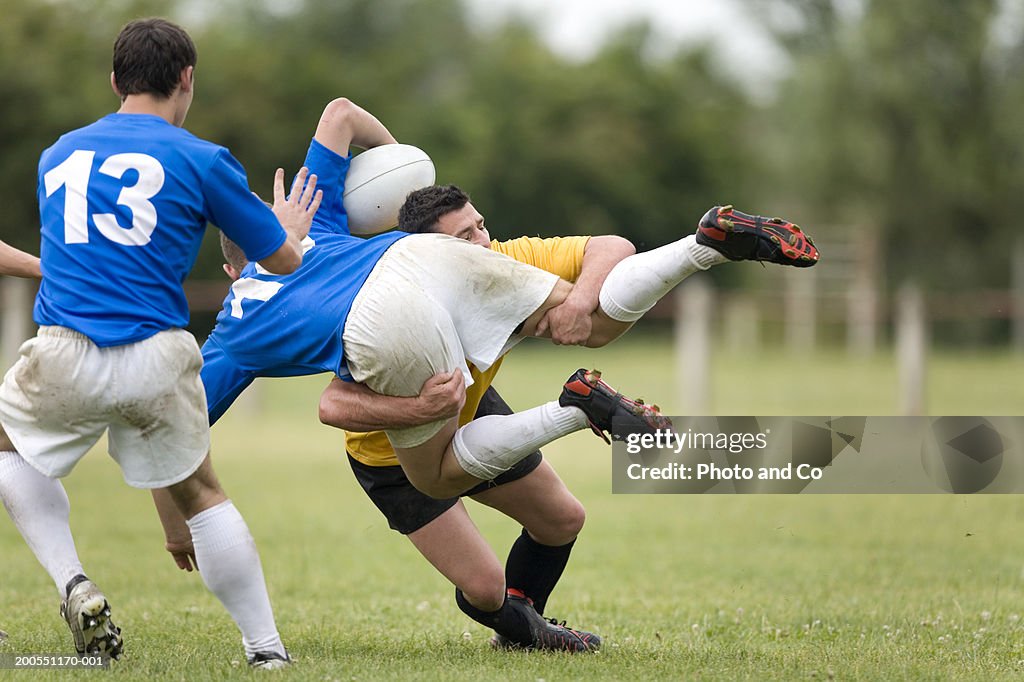 Young men playing rugby, one tackling opponent