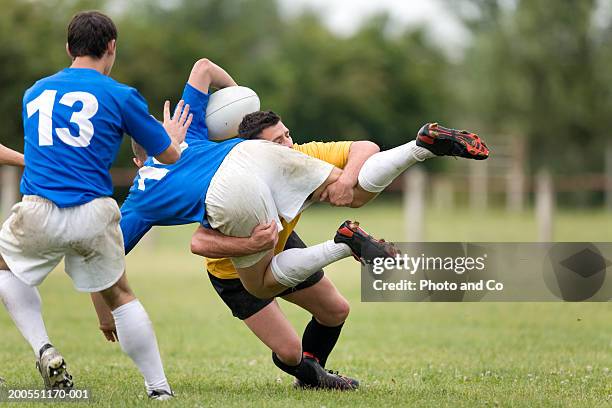 young men playing rugby, one tackling opponent - rugby tackling stock pictures, royalty-free photos & images