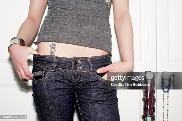 young woman with tattoo on stomach with hands in pockets, mid section - hipster trousers stock pictures, royalty-free photos & images