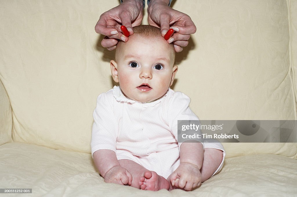 Baby girl (3-6 months) with hand placing candy on head