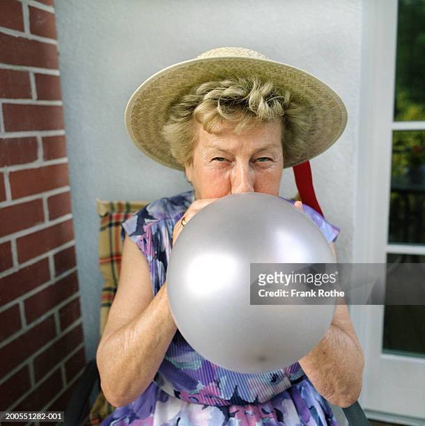 senior woman wearing straw hat, blowing balloon - blowing up balloon bildbanksfoton och bilder