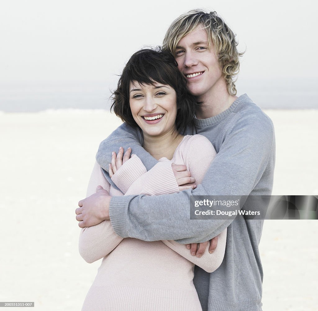 Young couple embracing on beach, smiling, portrait