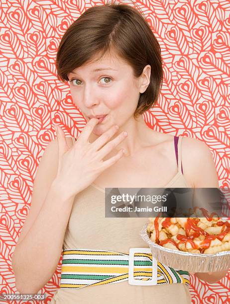 young woman licking finger eating french fries, smiling, portrait - finger in mouth stock pictures, royalty-free photos & images