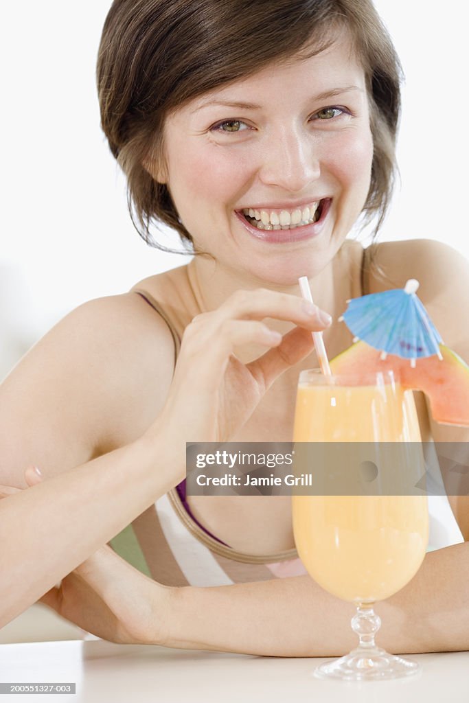 Young woman drinking orange juice, smiling, close-up, portrait