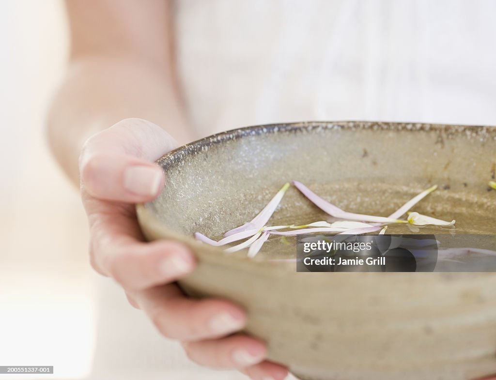 Woman holding bowl of petals in water, close-up, mid section