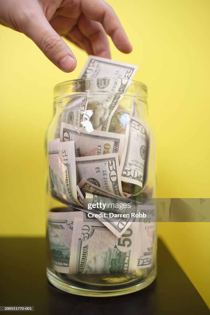 Hand reaching for US dollar bill from glass jar, close-up