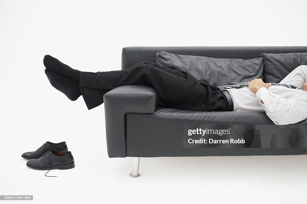 Businessman relaxing on sofa, low section, side view