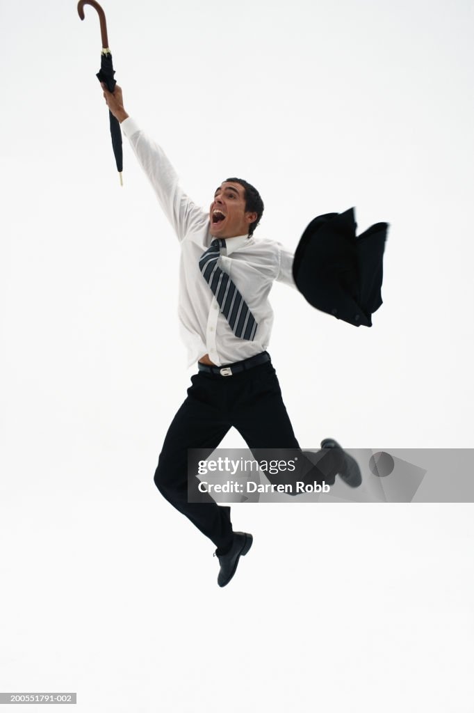 Young businessman holding coat and umbrella jumping, cheering