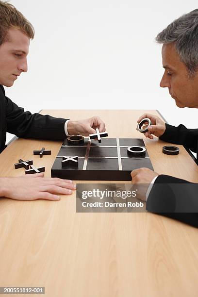 two businessmen playing noughts and crosses (tic tac toe) at office desk, side view - tic tac toe stock pictures, royalty-free photos & images