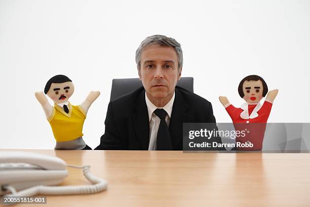 mature businessman sitting at desk, holding puppets, portrait - puppeteer stock pictures, royalty-free photos & images