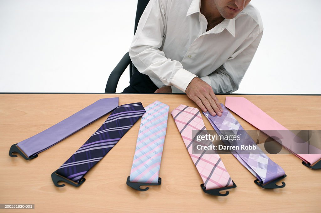 Businessman sitting by desk, choosing tie, mid section