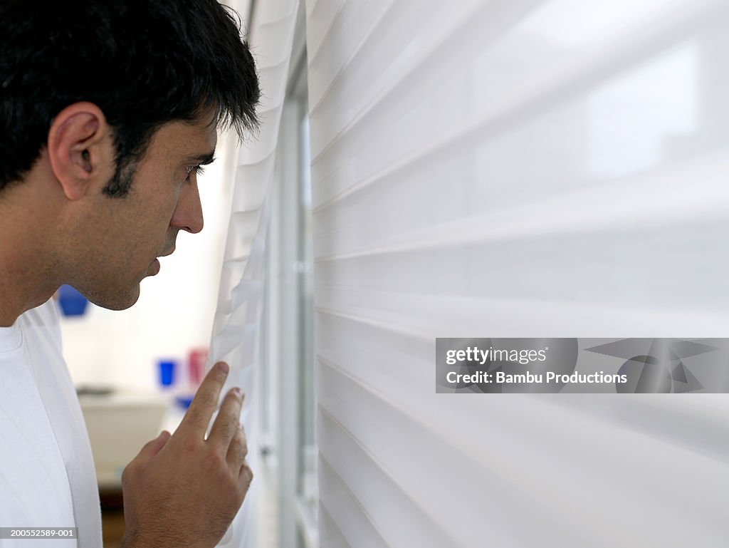 Mid adult man looking through blinds, close-up, side view