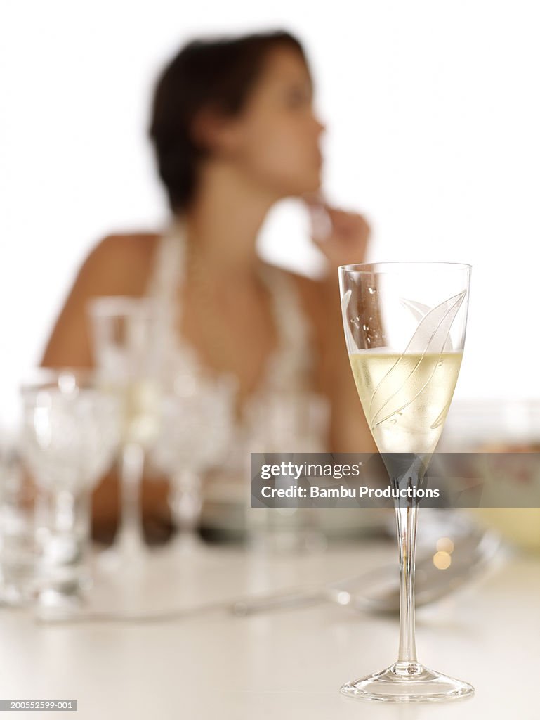 Woman sitting at dining table, focus on champagne flute at foreground