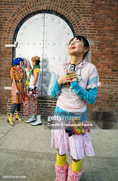 three women standing on sidewalk, woman with mobile in foreground - harajuku tokyo harajuku street fashion stock pictures, royalty-free photos & images