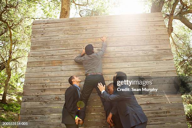 business colleagues helping man go over obstacle wall - klimmuur stockfoto's en -beelden