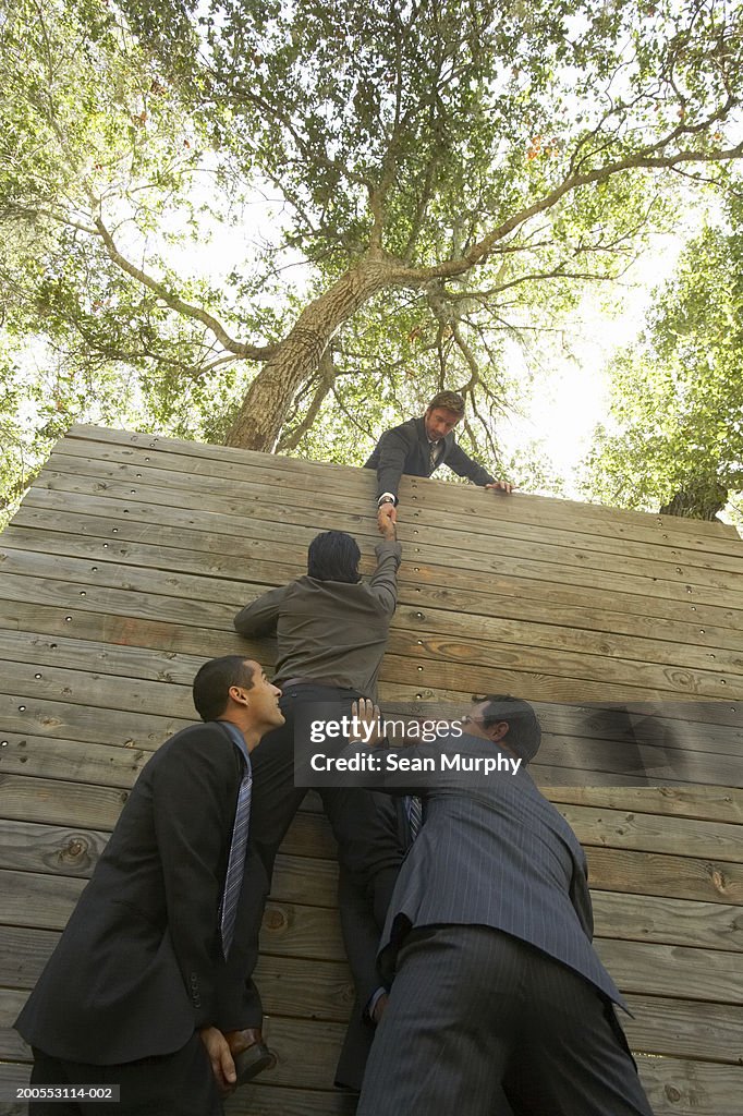 Business colleagues helping man go over obstacle wall, low angle view