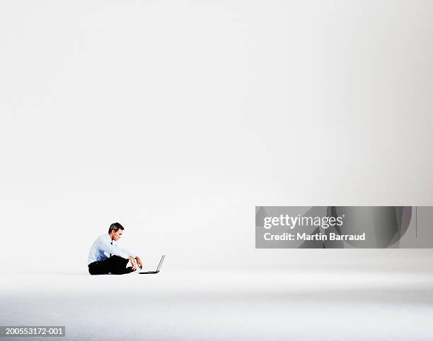 man sitting cross-legged, using laptop, side view - profile laptop sitting stock-fotos und bilder