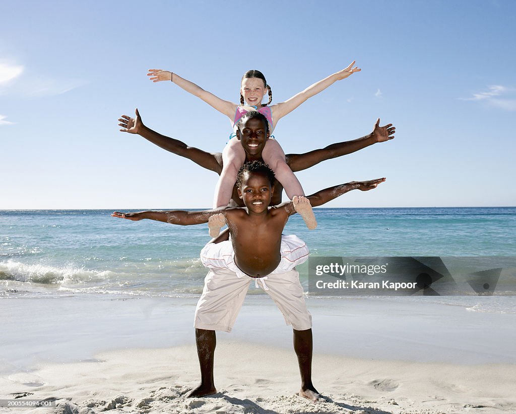 Boys and girl (8-15) doing balancing act on beach, smiling, portrait