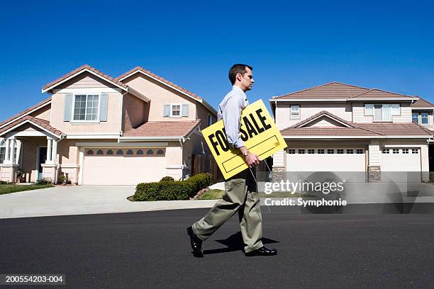 male estate agent walking in front of house with holding for sale sign, side view - estate agent sign stockfoto's en -beelden