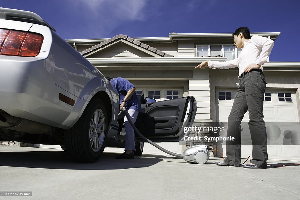 Man holding vacuum cleaner leaning in to car, low angle view