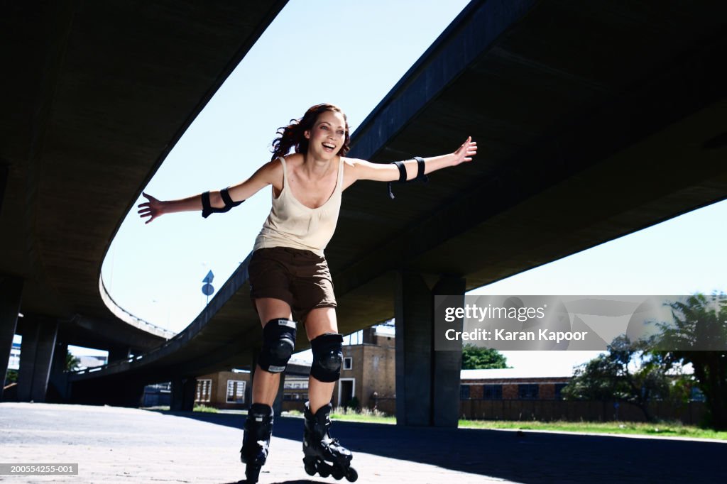 Young woman inline skating, smiling, low angle view