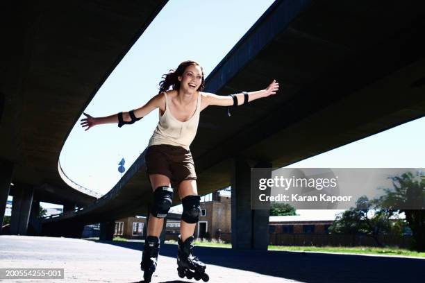 young woman inline skating, smiling, low angle view - roller en ligne photos et images de collection