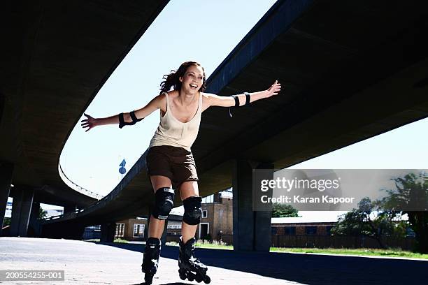 young woman inline skating, smiling, low angle view - rolschaatsen schaats stockfoto's en -beelden