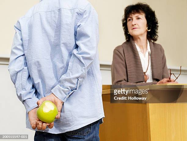 boy (8-9) hiding apple from teacher - mani dietro la schiena foto e immagini stock